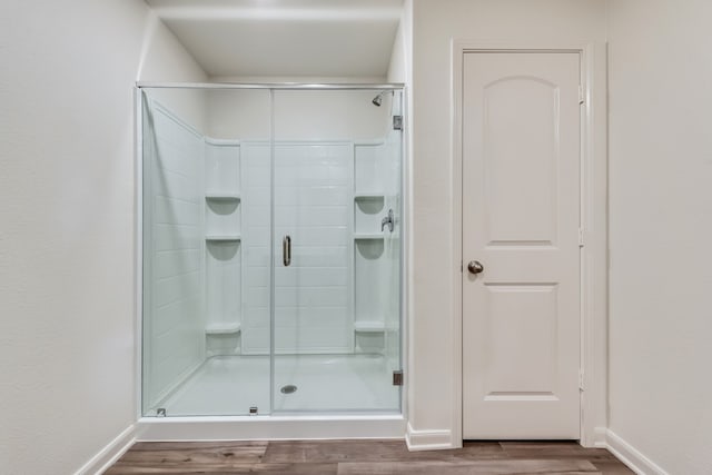 full bathroom featuring baseboards, wood finished floors, and a shower stall