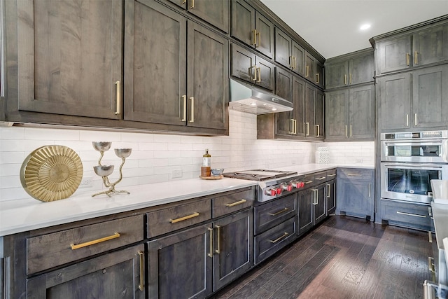 kitchen featuring light countertops, stainless steel appliances, backsplash, dark wood-type flooring, and under cabinet range hood