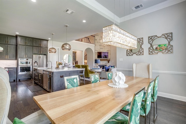 dining space featuring visible vents, arched walkways, dark wood finished floors, and ornamental molding