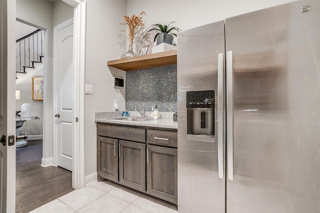 kitchen featuring open shelves, dark brown cabinetry, light tile patterned flooring, stainless steel fridge, and a sink