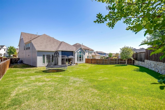 back of property featuring a fenced backyard, a trampoline, central AC, and a yard