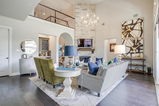 living room with dark wood-style flooring, visible vents, a towering ceiling, arched walkways, and a chandelier