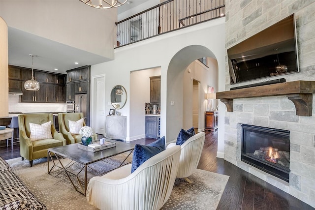 living area with dark wood-style flooring, arched walkways, a high ceiling, and a fireplace