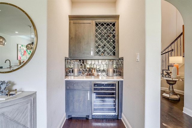 bar featuring baseboards, indoor wet bar, dark wood-style flooring, and beverage cooler
