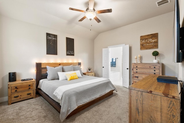 bedroom featuring ceiling fan, light colored carpet, visible vents, vaulted ceiling, and ensuite bathroom