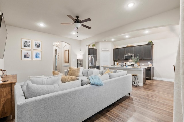 living area featuring light wood-style floors, arched walkways, ceiling fan, and recessed lighting