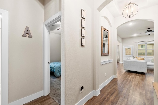 corridor featuring arched walkways, baseboards, an inviting chandelier, and wood finished floors