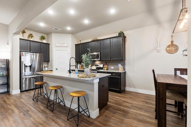kitchen with a sink, a kitchen breakfast bar, an island with sink, stainless steel appliances, and visible vents