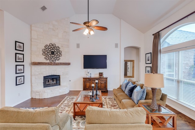 living room featuring ceiling fan, a stone fireplace, visible vents, arched walkways, and high vaulted ceiling