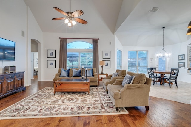 living room featuring visible vents, arched walkways, wood finished floors, high vaulted ceiling, and ceiling fan with notable chandelier