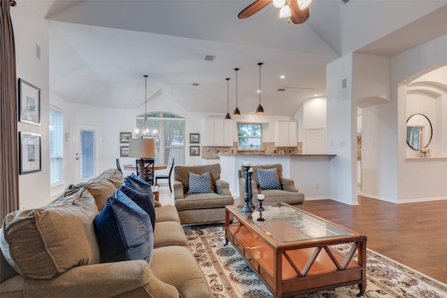 living room with visible vents, arched walkways, ceiling fan with notable chandelier, light wood-type flooring, and vaulted ceiling