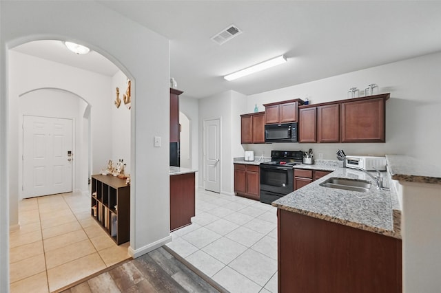 kitchen featuring black appliances, a sink, arched walkways, and light stone countertops