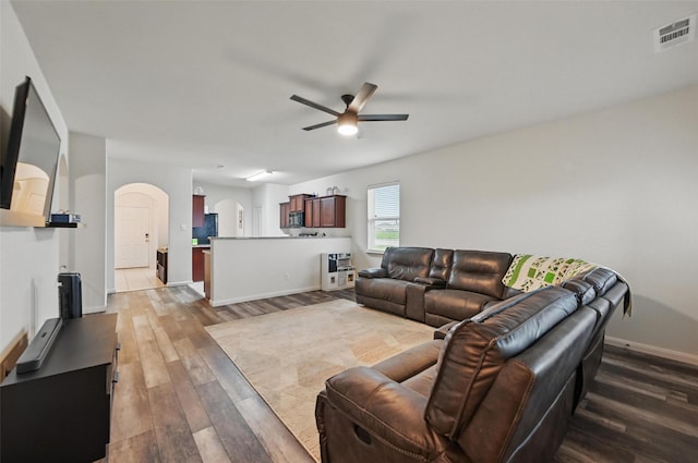 living area with ceiling fan, arched walkways, wood finished floors, and baseboards