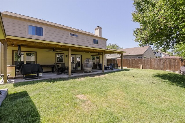 rear view of property with ceiling fan, a chimney, fence, a yard, and a patio