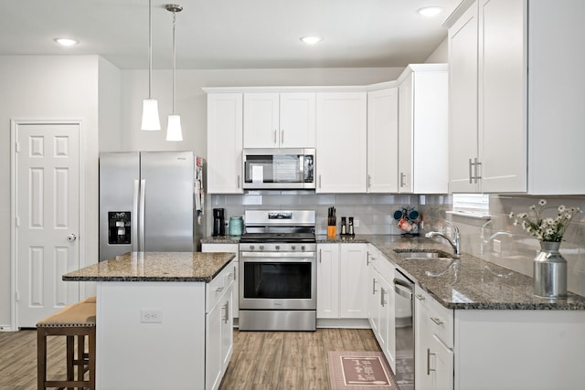 kitchen featuring appliances with stainless steel finishes, a sink, light wood-style flooring, and a center island