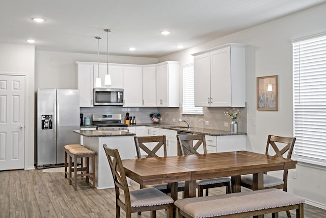 kitchen with backsplash, appliances with stainless steel finishes, a center island, light wood-type flooring, and white cabinets