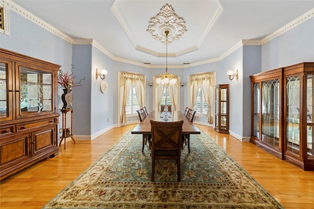 dining room with a tray ceiling, an inviting chandelier, baseboards, and light wood-style floors