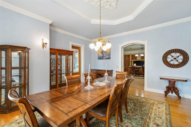 dining space with light wood-style floors, arched walkways, and ornamental molding