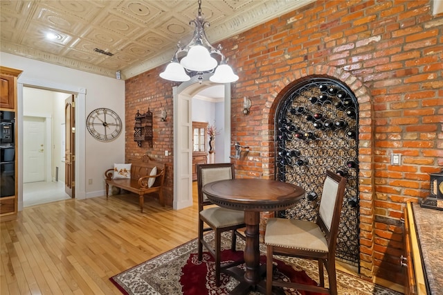 dining area with light wood finished floors, arched walkways, brick wall, baseboards, and visible vents