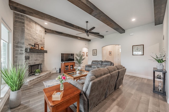 living room with a fireplace, arched walkways, a ceiling fan, baseboards, and wood finished floors