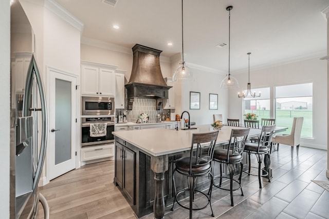 kitchen with a breakfast bar area, premium range hood, stainless steel appliances, decorative backsplash, and a center island with sink