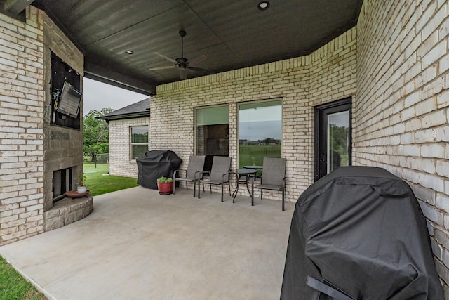 view of patio with a ceiling fan, area for grilling, and an outdoor brick fireplace