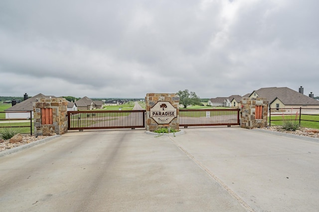 view of road featuring a gate, a gated entry, curbs, and a residential view