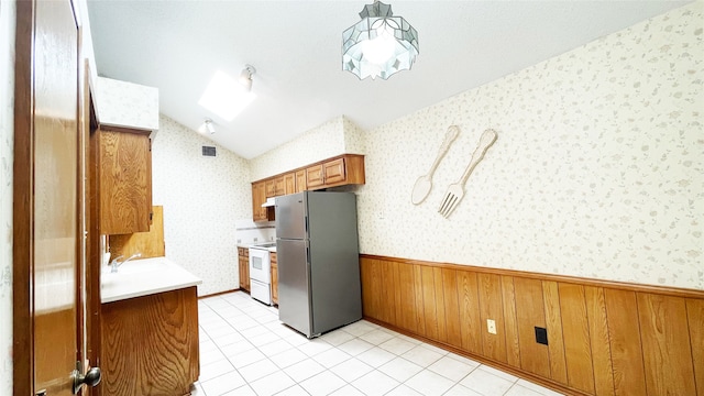 kitchen with brown cabinetry, freestanding refrigerator, wainscoting, and wallpapered walls