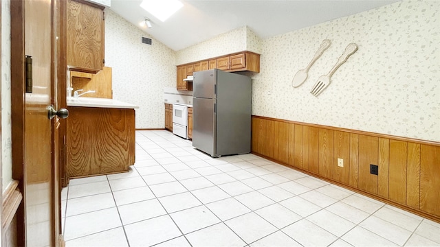 kitchen with wainscoting, light countertops, brown cabinetry, freestanding refrigerator, and visible vents