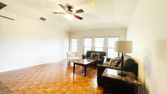 living room with visible vents, baseboards, a textured ceiling, a ceiling fan, and vaulted ceiling