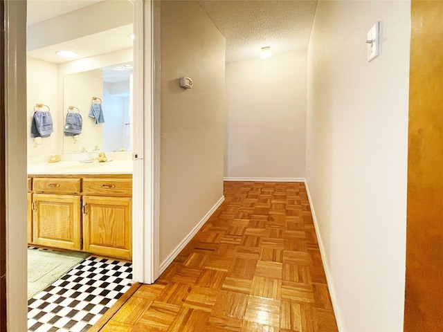 hall with baseboards, a sink, and a textured ceiling