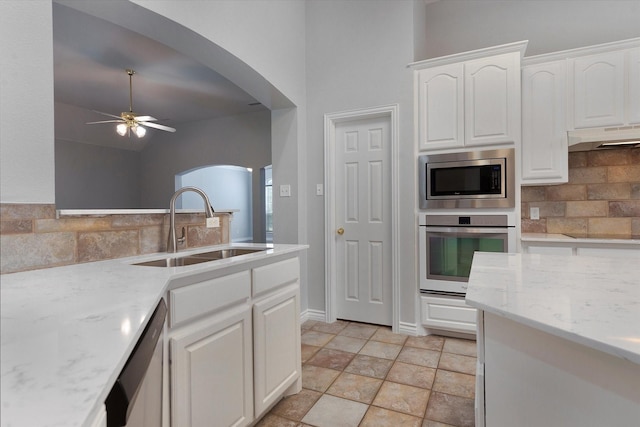 kitchen with ceiling fan, appliances with stainless steel finishes, a sink, arched walkways, and backsplash