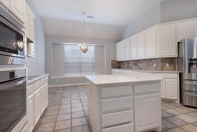 kitchen featuring an inviting chandelier, stone tile floors, stainless steel appliances, lofted ceiling, and tasteful backsplash