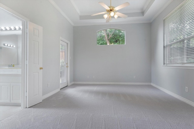 empty room with crown molding, baseboards, light colored carpet, a raised ceiling, and a ceiling fan