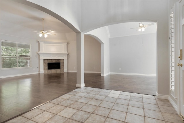 unfurnished living room with a ceiling fan, built in shelves, light wood-style flooring, and a tile fireplace