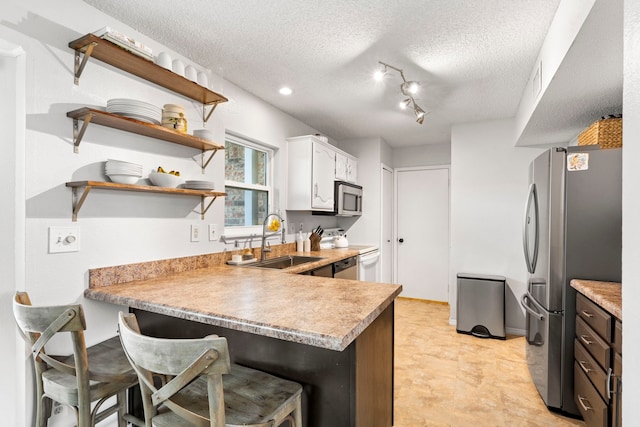4145 Malone Ave, The Colony, TX 75056 - kitchen featuring appliances with stainless steel finishes, a breakfast bar, a sink, a textured ceiling, and a peninsula