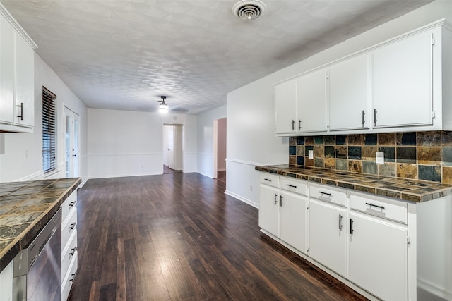 kitchen featuring stainless steel dishwasher, decorative backsplash, white cabinetry, and dark wood-style floors