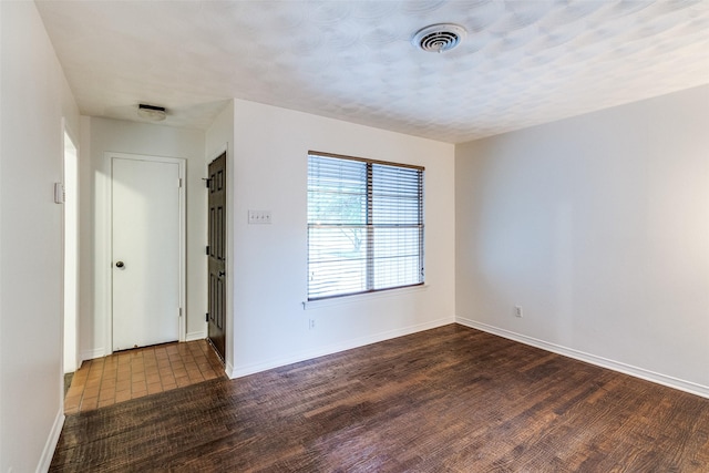 unfurnished room featuring visible vents, baseboards, and dark wood-type flooring