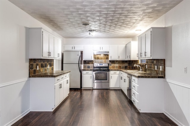 kitchen with a sink, appliances with stainless steel finishes, under cabinet range hood, and dark countertops