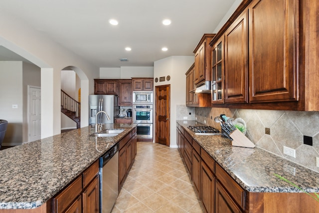 1306 Andrew Ct, Lewisville, TX 75056 - kitchen featuring appliances with stainless steel finishes, a sink, arched walkways, glass insert cabinets, and backsplash