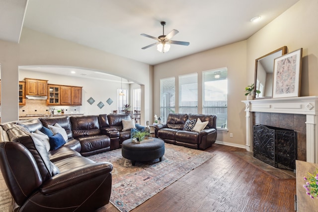 1306 Andrew Ct, Lewisville, TX 75056 - living room with a ceiling fan, arched walkways, dark wood-style flooring, a tiled fireplace, and baseboards