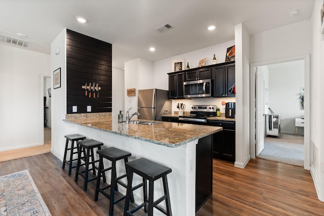 kitchen featuring appliances with stainless steel finishes, a sink, a breakfast bar area, visible vents, and dark wood-style floors