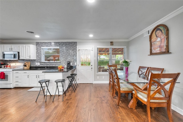 dining space with crown molding, baseboards, wood finished floors, and visible vents