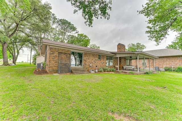 rear view of house featuring brick siding, central air condition unit, a yard, and a chimney