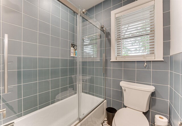 full bath featuring toilet, tile walls, and combined bath / shower with glass door