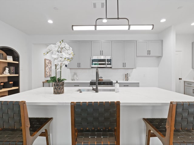 kitchen featuring stainless steel microwave, a breakfast bar, light stone countertops, and visible vents