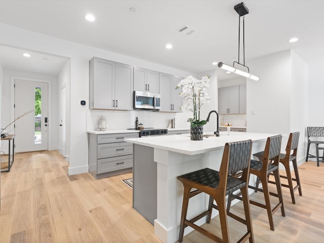 kitchen featuring a kitchen breakfast bar, light countertops, stainless steel microwave, range with electric cooktop, and gray cabinetry
