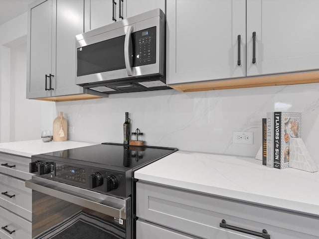 kitchen featuring backsplash, stainless steel microwave, and black electric range oven