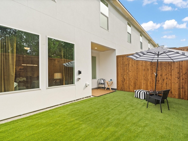 back of house featuring a lawn, fence, and stucco siding