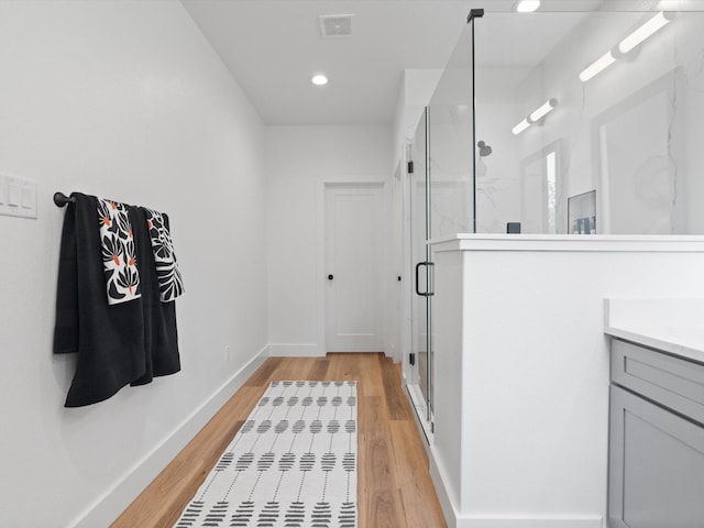 interior space with visible vents, a marble finish shower, wood finished floors, and vanity